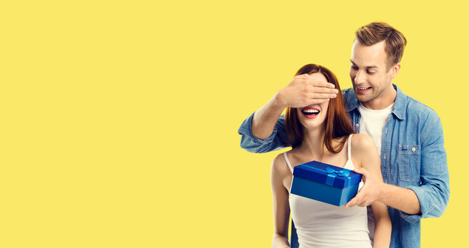 Love, dating, celebrating, lovers concept - happy amorous couple with blue gift box. Yellow background. Copy space for some text.