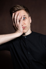 A man in round glasses and a black shirt is grimacing