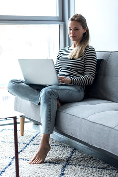 Pretty young woman using her laptop while sitting on sofa at home.
