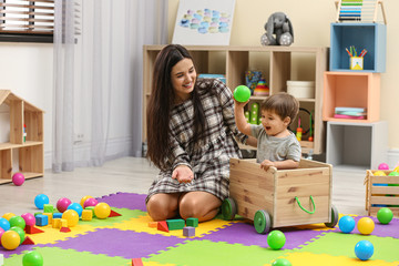 Young nanny and cute little baby playing with toys at home - obrazy, fototapety, plakaty