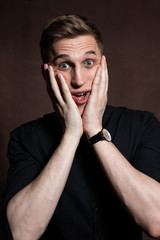 A man in round glasses and a black shirt is grimacing