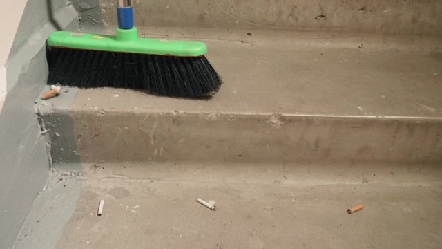 Green broom sweeps cigarette butts off stairs