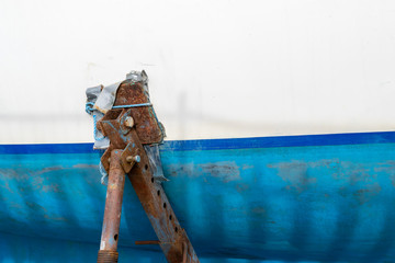 Image featuring a rusty boat stand propping up a boat with a blue and white horizontally painted...