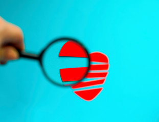 Red broken heart made of paper under a magnifying glass on a blue background with copy space. Symbol of love. Concept of unsuccessful love or disappointment in love. Soft focus