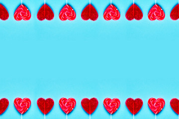 Valentines Day background. Frame from red lollipop candies heart shape on blue background. Flat lay, copy space