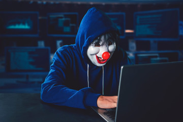 Hacker wearing clown mask hacking on a laptop computer
