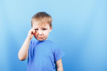 Upset crying sad boy at blue background, looking at camera.