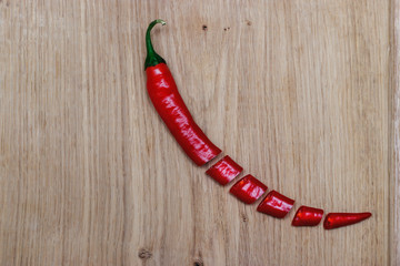 A long red chili pepper cut in equal parts lies on a white oak board. Still life in the kitchen...