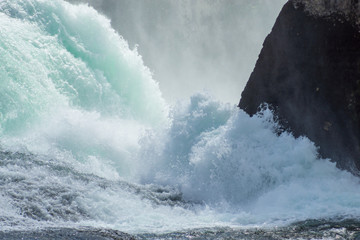 The roaring waters of the Rhine Falls between the rocks.