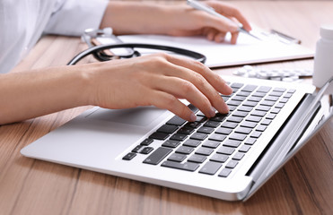 Fototapeta premium Doctor working with laptop at desk in office, closeup. Medical service