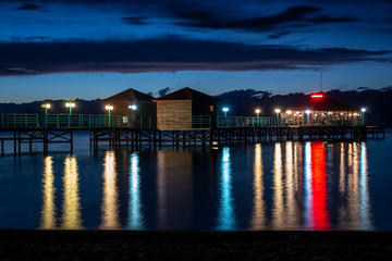 Night pier with colorful reflections on water and cloudy sky background.