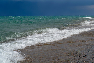 Stormy clouds with waves in the sea and pebble beach.