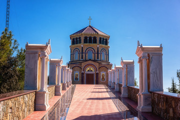 Fototapeta premium Way to the orthodox church at the hill Panayia Sto Throni over the famous Kykkos monastery, Cyprus. Beautiful architectural landmark on a sunny day, pilgrimage and travel background