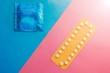 Contraception pills and condom on blue and pink background. Male and female contraceptives concept. Bitrh control concept.