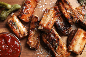 Delicious grilled ribs with sauce on wooden table, flat lay