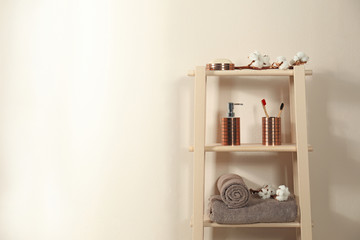 Wooden shelving unit with toiletries near beige wall indoors, space for text. Bathroom interior element