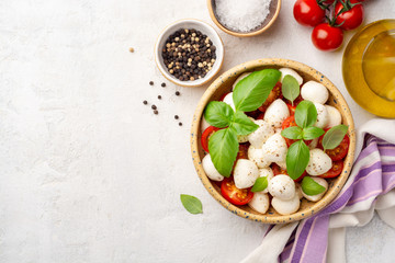 Traditional Italian caprese salad with mozzarella cheese, cherry tomatoes and basil in ceramic bowl on concrete background. Top view, copy space.