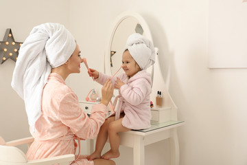 Young mother and little daughter doing makeup at dressing table