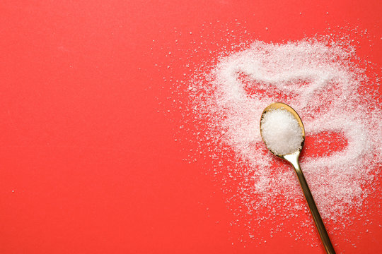 Granulated sugar and spoon on red background, flat lay. Space for text