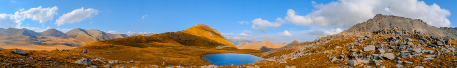Obraz premium Panoramic view on mountains with mountain lake and blue sky. Beautiful alpine landscape. Rural scenery.