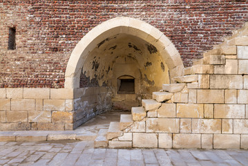 Exterior of ancient brick building with shabby stone stairway and crumbling arched alcove on street