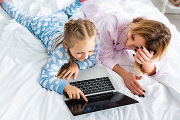 overhead view of smiling mother and daughter pointing with finger at laptop