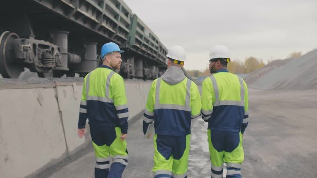 Diverse industrial employees on industrial railway platform controlling crushed stone upload.
