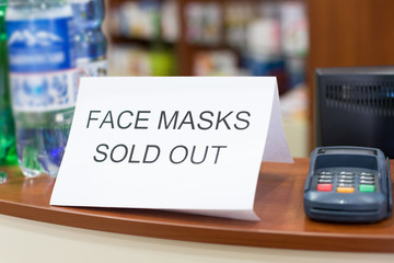 Information plate on counter in pharmacy with text: face masks are sold out, not in stock. Epidemic of N-CoV 2019 influenza coronavirus mutated and spreading in China. Bank card payment terminal