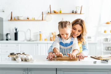 smiling mother and cute daughter rolling dough on table