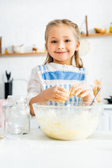 smiling and cute kid in apron cooking dough in kitchen