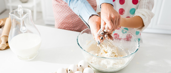 Cropped view of mother and daughter kneading dough together in bowl