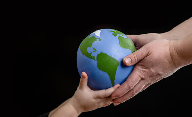 Close up hands of mother gives the planet into the hands of a child. Isolated on dark background. Empty space for text