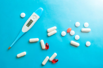 Thermometer showing high body temperaturep and pills on blue background. Flu cold concept. Healthcare medical concept. Medicine pill. Emergency medical treatment. Disease treatment.
