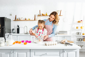 Fototapeta na wymiar Beautiful attractive mother standing behind cute daughter while kneading dough