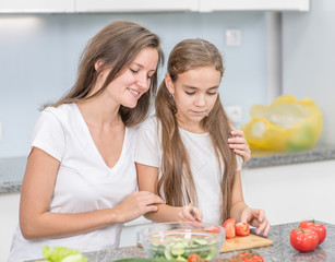 Happy family at home. Mother teaches her daughter to cut vegetables for dinner