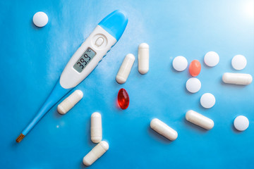 Thermometer showing high body temperaturep and pills on blue background. Flu cold concept. Healthcare medical concept. Medicine pill. Emergency medical treatment. Disease treatment.