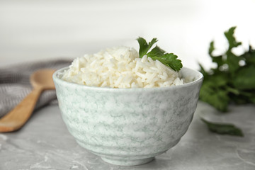 Bowl with tasty cooked rice and parsley on light grey marble table, closeup