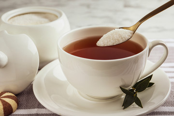 Spoon with granulated sugar over cup of tea on table
