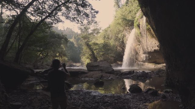 A young adventure and nature photographer taking pictures of a waterfall from a cave in the middle of the jungle