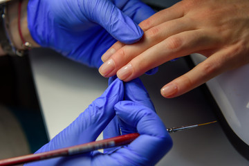 Applying a transparent base coat to the client's nail with a thin brush in manicure salon. Correct glare on the nail plate, close-up.