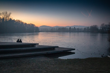 silhouette of couple people enjoying sunset view on freezing cold lake, slovenia