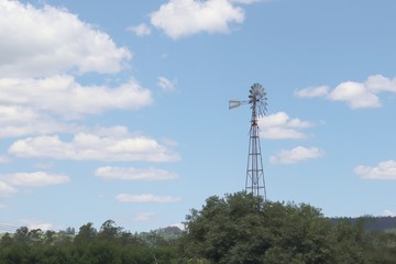 View of the blue sky with white clouds and a large metal pinwheel surrounded by trees