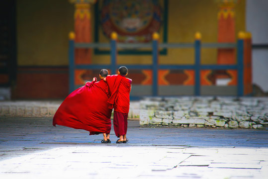 Konigreich Bhutan, Asien, Himalaya. Zwei junge Novizen in Innenhof eines Kloster laufen umarmt zum Tempel. Ihre roten Gew&auml;nder leuchten in der Sonne und wehen im Wind.