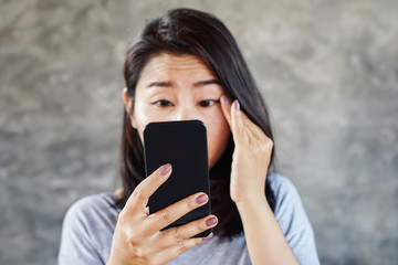 Asian woman having problem with eye squints watching mobile phone screen  