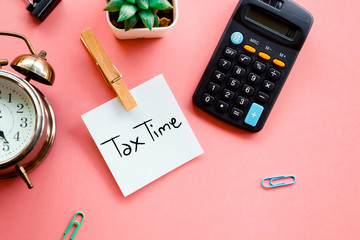 tax time concept on sticky note, calculator and clock on pink background