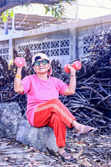 Obraz na płótnie Canvas Cheerful elderly person lady exercising for Good health strong and long life. Happy active lifestyle of old woman grandmother concept. Trendy Asian Thai Senior Female sitting holding weight dumbbells.