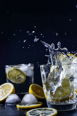 Fototapeta na wymiar splash Gin and tonic cocktail with lemon slices Ice cube falls into water with lemon Copy space, lemonade