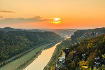 Fototapeta premium Saxon Switzerland National Park with the Elbe Valley.. Landscape with a view from Bastei Bridge with the Elbe and rocks, trees and forests in the autumn mood with an orange horizon at sunset