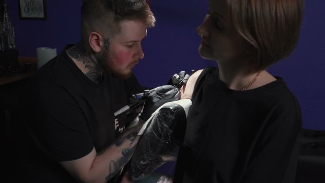 Shooting of man doing black tattoo of snake for woman