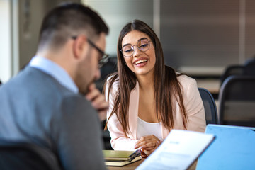 Portrait of young  female client or candidate sitting at table, talking to male manager and smiling in office. Job interview or consultancy concept. Young attractive woman during job interview - obrazy, fototapety, plakaty